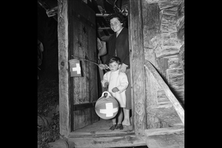 Mutter und Kind mit Lampions stehen in einem Türrahmen eines Holzhauses