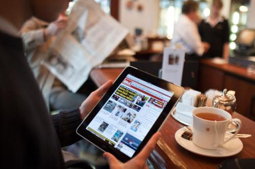 Man holding iPad, reading news, in a cafe